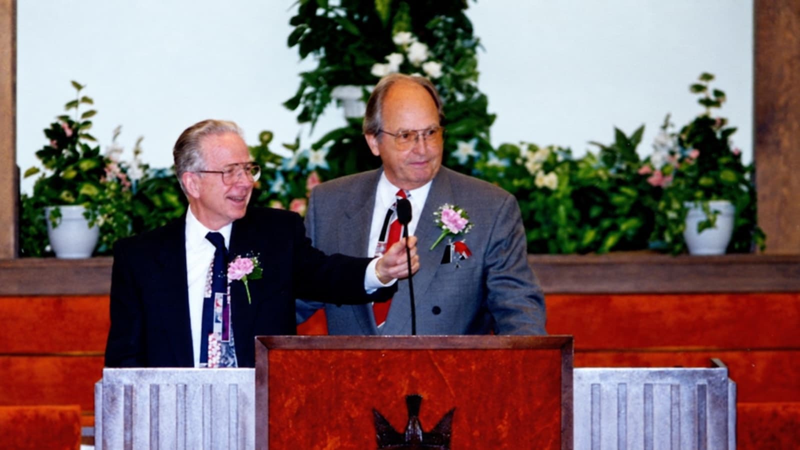 Two ministers in suits and boutonnieres standing together at the pulpit.