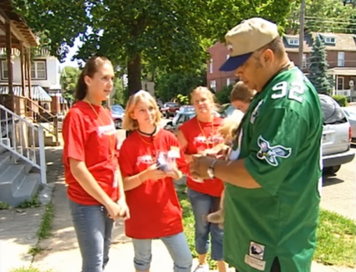 Young outreach volunteers in red shirts talking with a man on a city sidewalk.